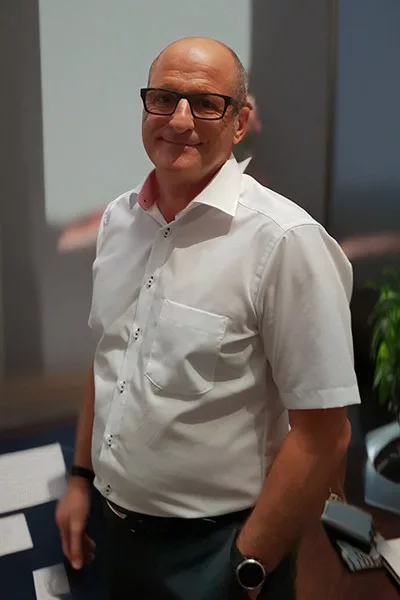 Mann mit Brille und weißem Hemd lächelt.